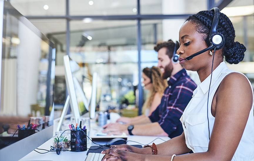 Women and man with headsets at desktops in a call center using AppDynamics in Cisco Unified Contact Center Enterprise (UCCE)