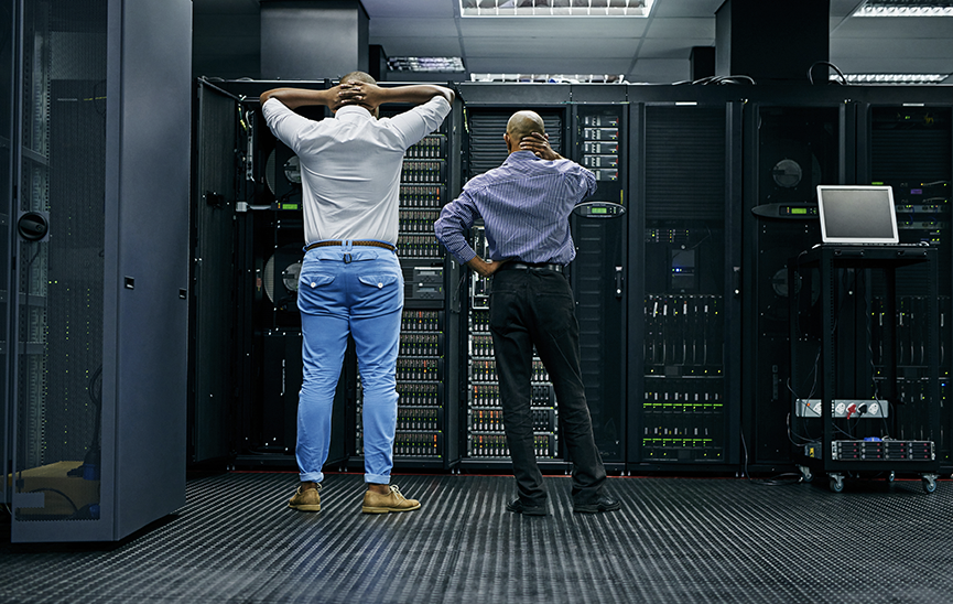 Men standing in a server room facing racks and worrying about application outages and service outages