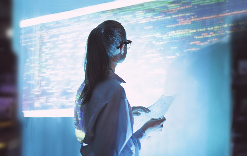 Woman standing in front of a large screen monitoring applications using full-stack observability